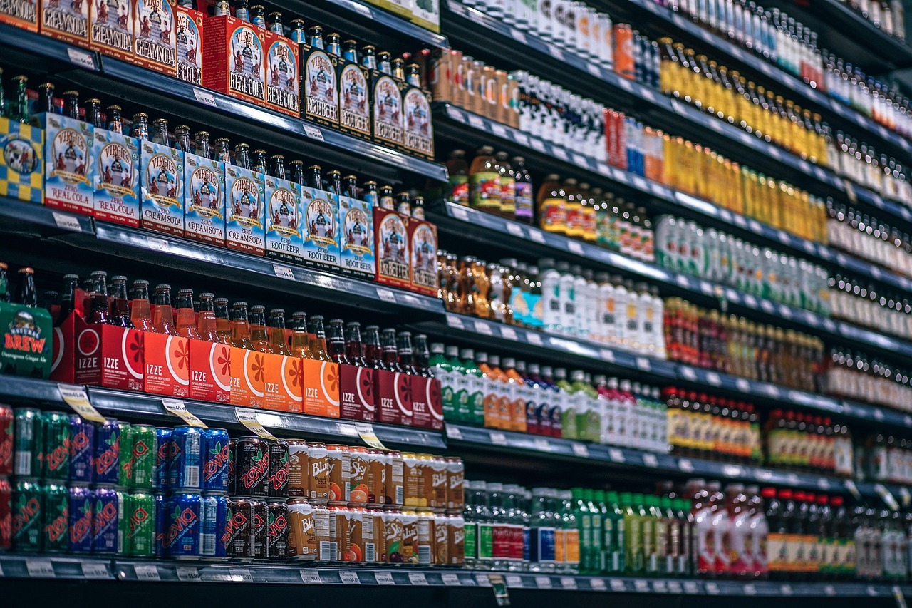 Supermarket beverage shelf stacked with bottled and canned drinks