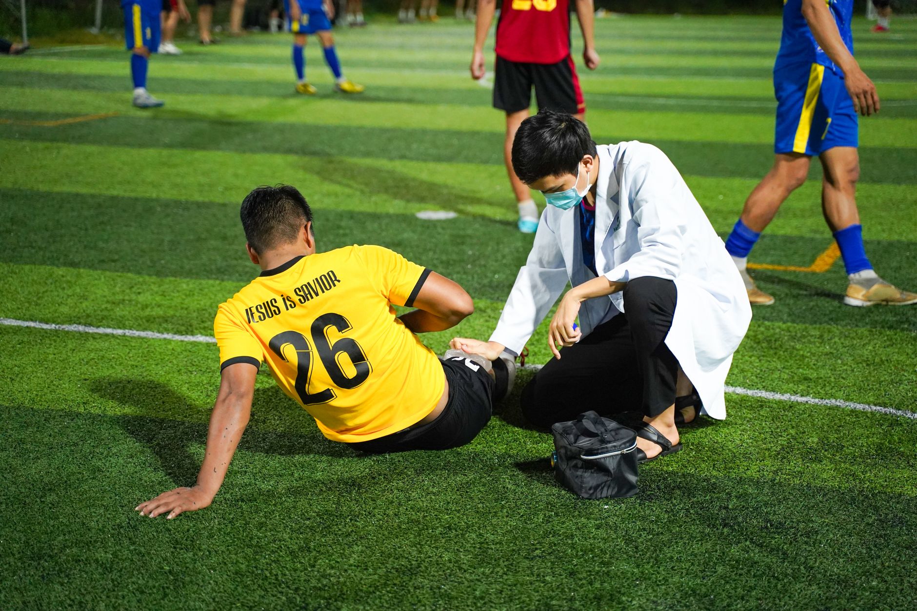 A medic attends to an injured player on a football field during a community match.