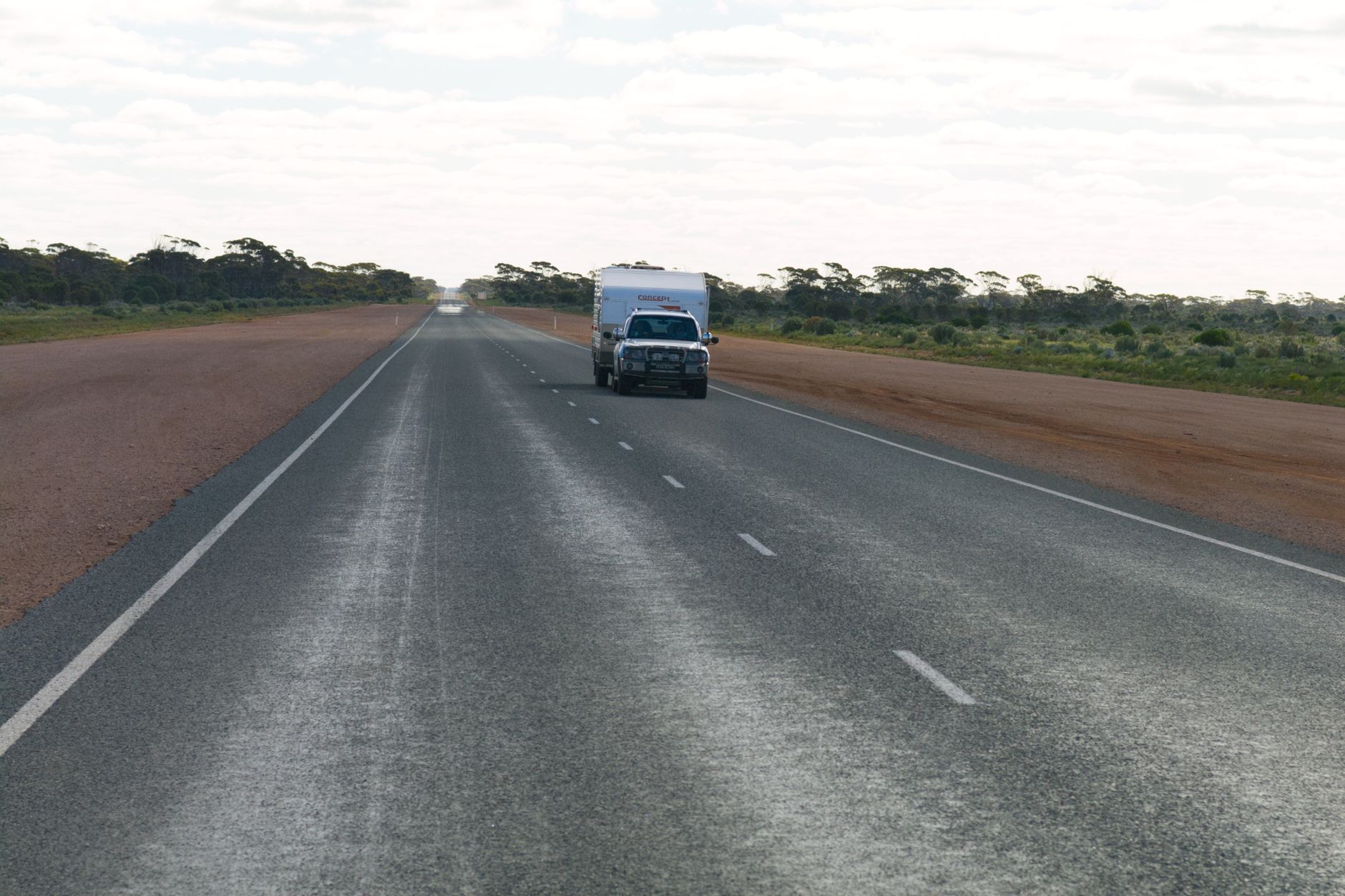 A single vehicle on a lonely outback road under a wide cloudy sky