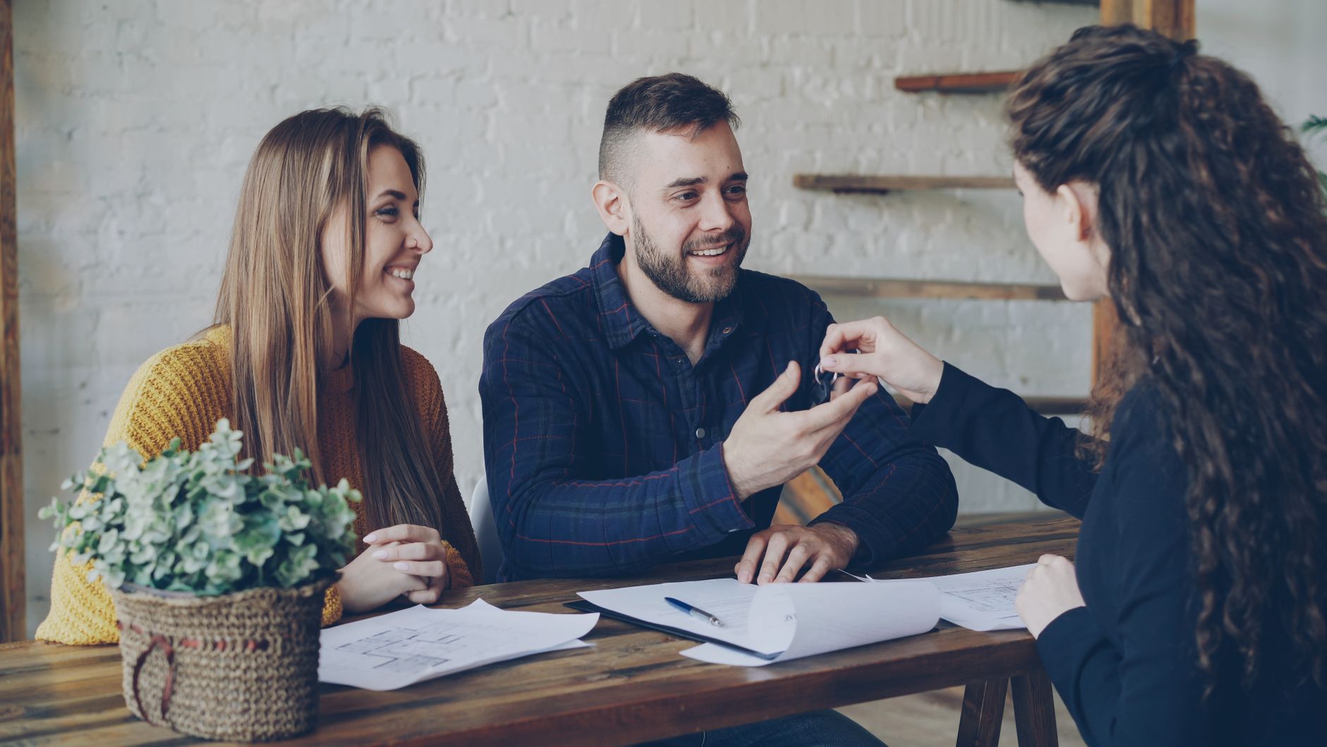 A couple receive house keys from a real estate agent at a desk after buying a home.