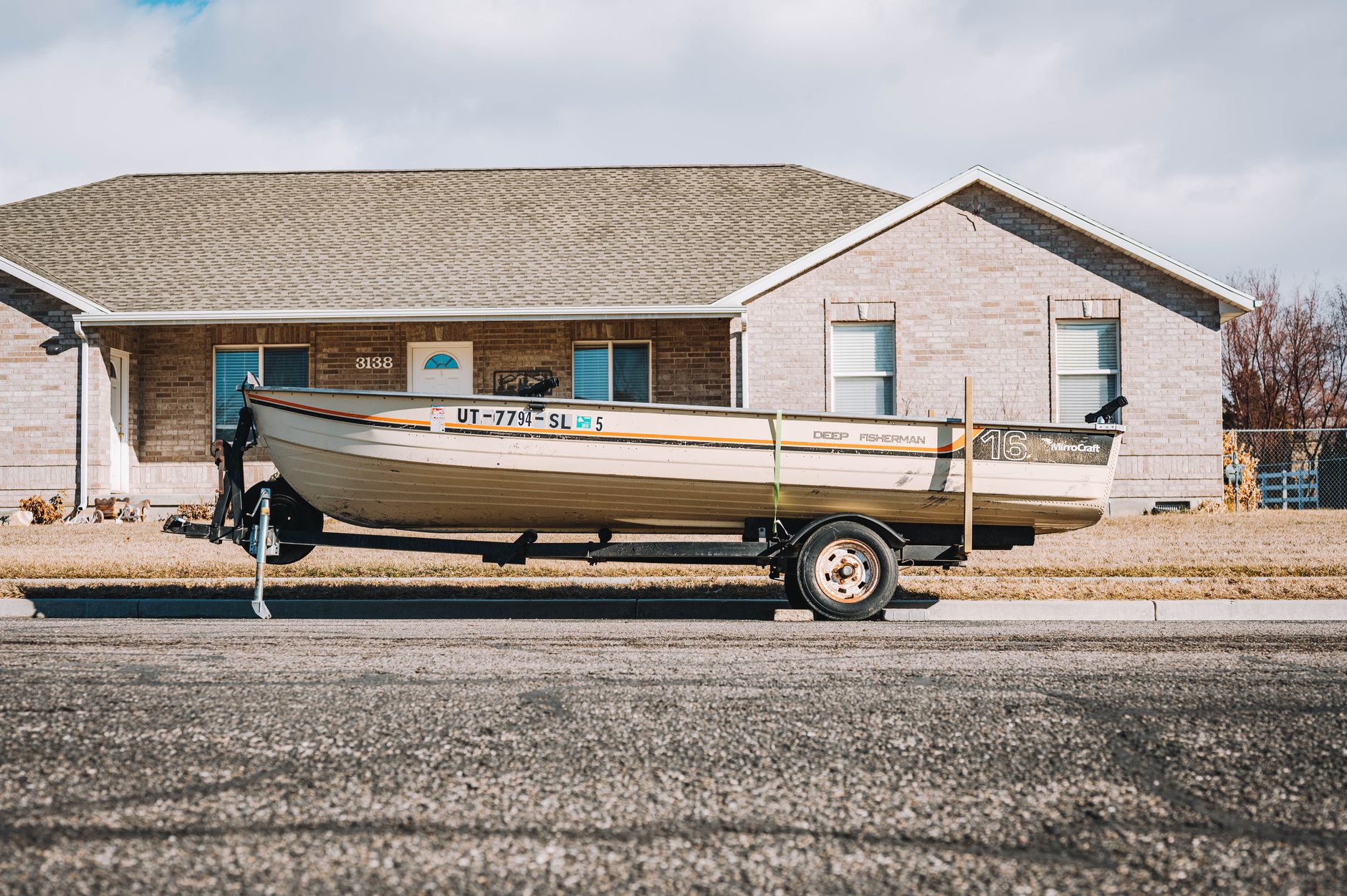 Small fishing boat on a trailer parked outside a suburban home