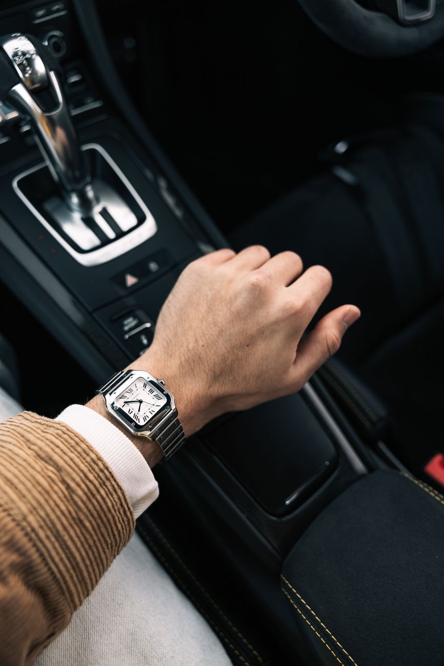 Luxury watch resting on a car gearshift, a clean stand-in for the Cartier Roadster's motorsport-flavoured design.
