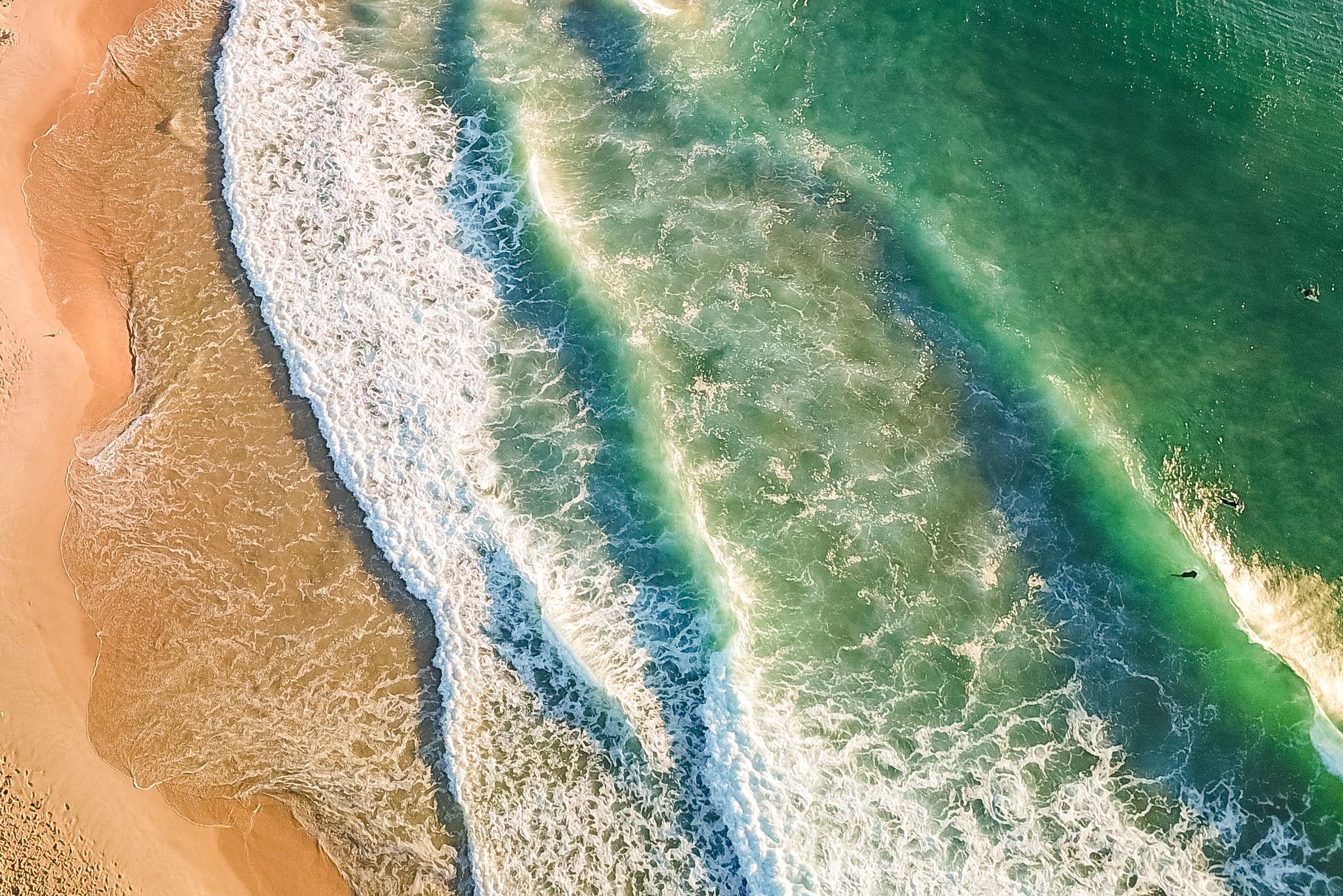 Aerial view of surf rolling onto a wide sandy beach on the NSW coast