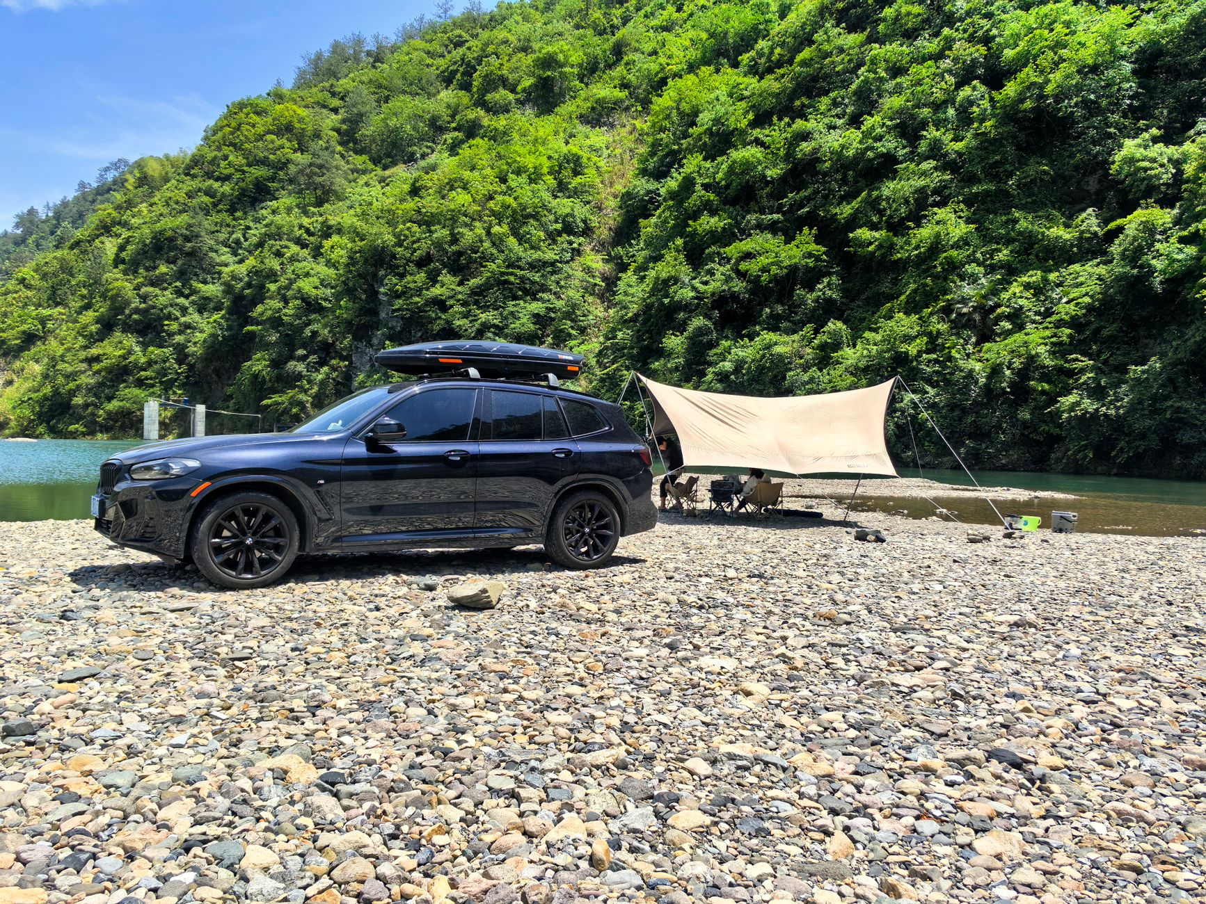 Black SUV parked beside a river campsite, matching the loaded-wagon camping angle of the Subaru axle-label recall story.