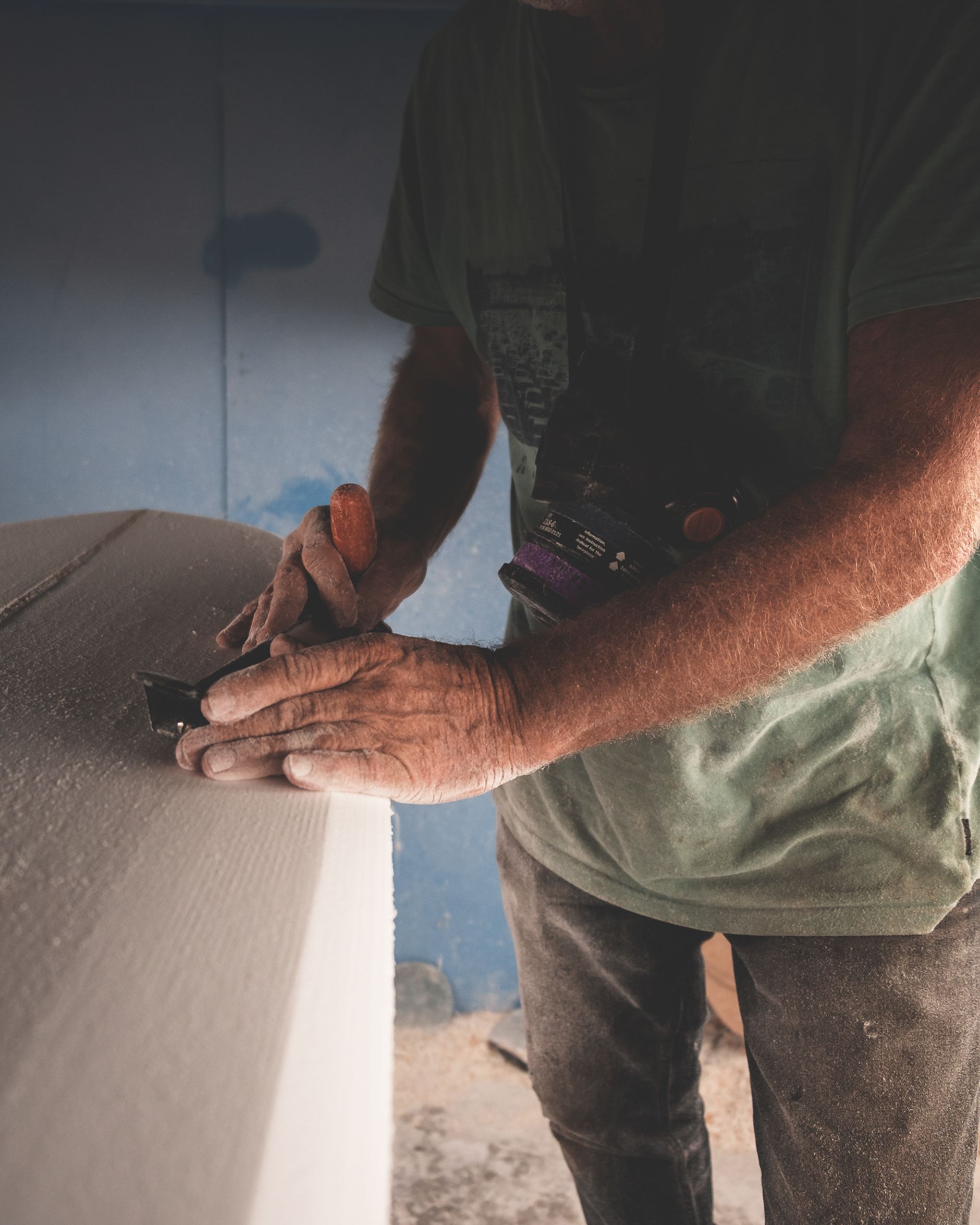 A hand plane smoothing a wooden surfboard blank in a workshop, echoing the craft side of Kyra Jonsun's legacy