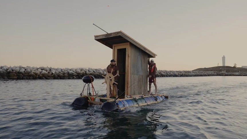 Two men aboard a barge with an old fashioned toilet and a barbecue on it