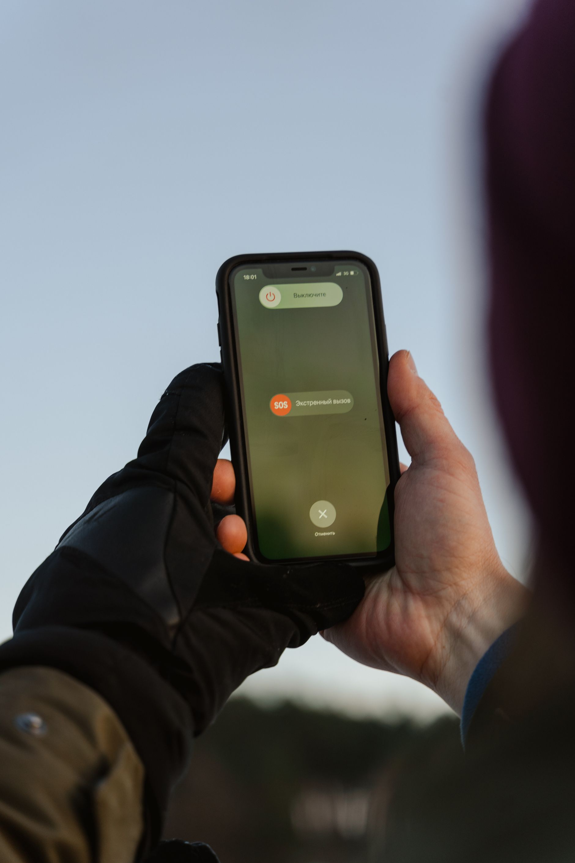 Person with gloves holding a smartphone outdoors during an emergency call
