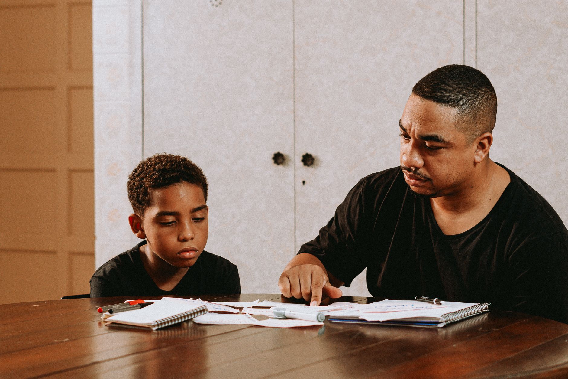 Father helping his son with homework at the dining table while reviewing school results together.