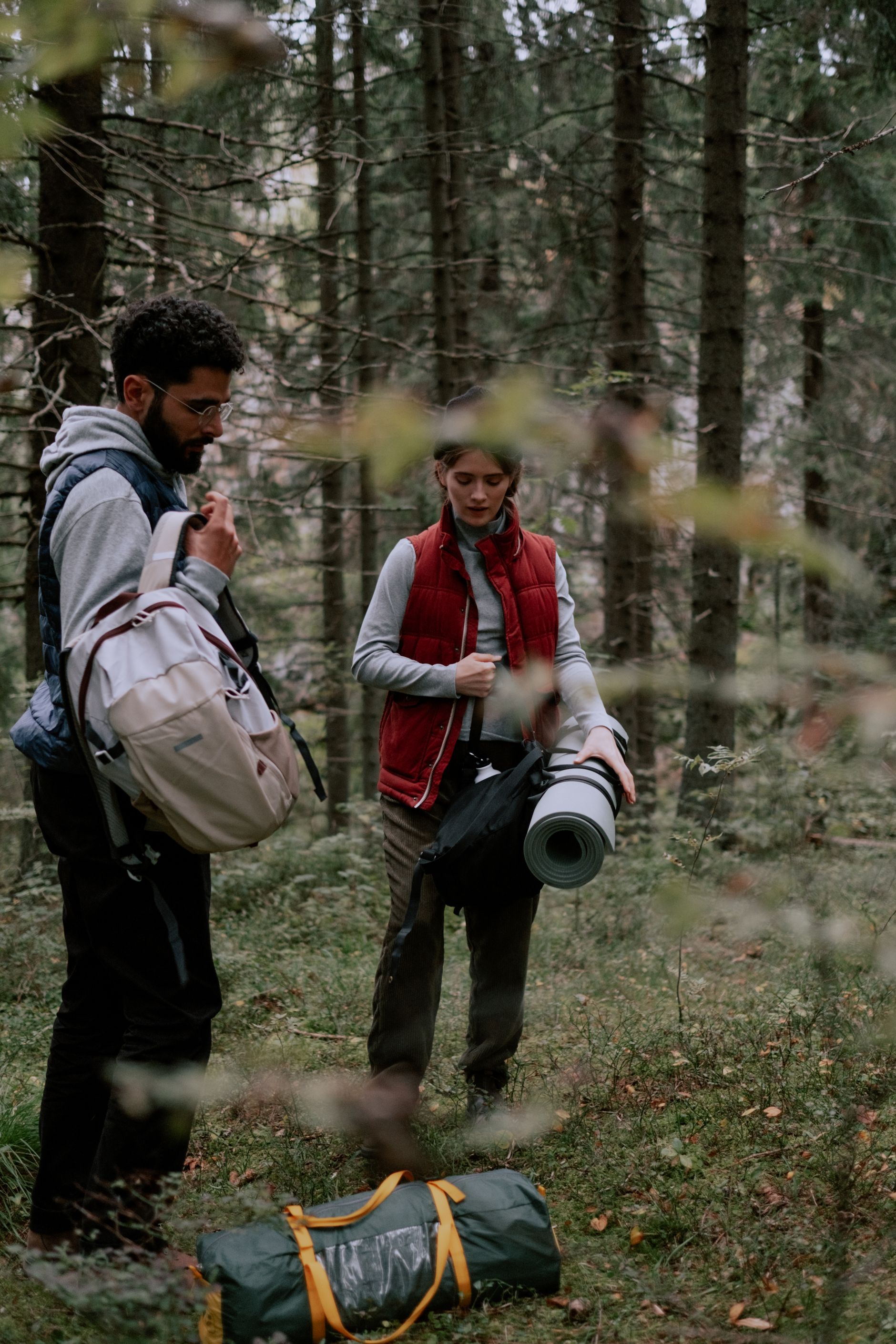 Camper carrying a rolled sleeping mat into a bush campsite before a cold overnighter