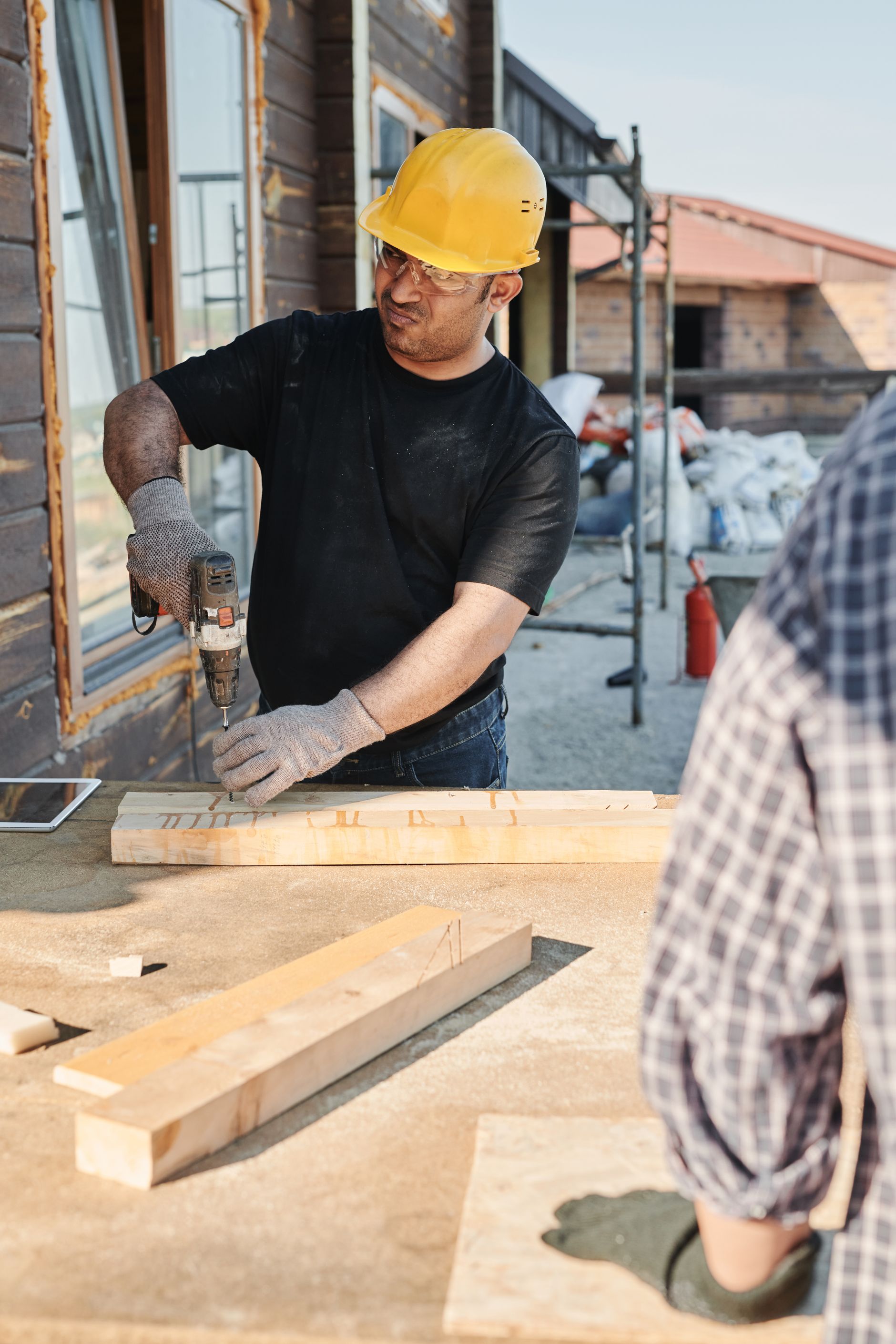 Construction worker using a drill on timber at an outdoor building site